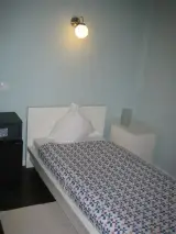 Cama individual iluminada por una lámpara de pared con la mininevera a un lado